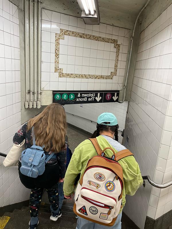 Watching two students wearing backpacks walk down the stairs into a subway station.
