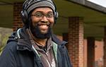 Photo of Anastasio Bonhomme smiling for camera on Landmark College quad. He is wearing a wool hat and headphones. 