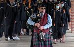 一名男子吹着风笛，穿着苏格兰裙，领着戴着毕业帽、身穿毕业服的学生走向毕业典礼场地