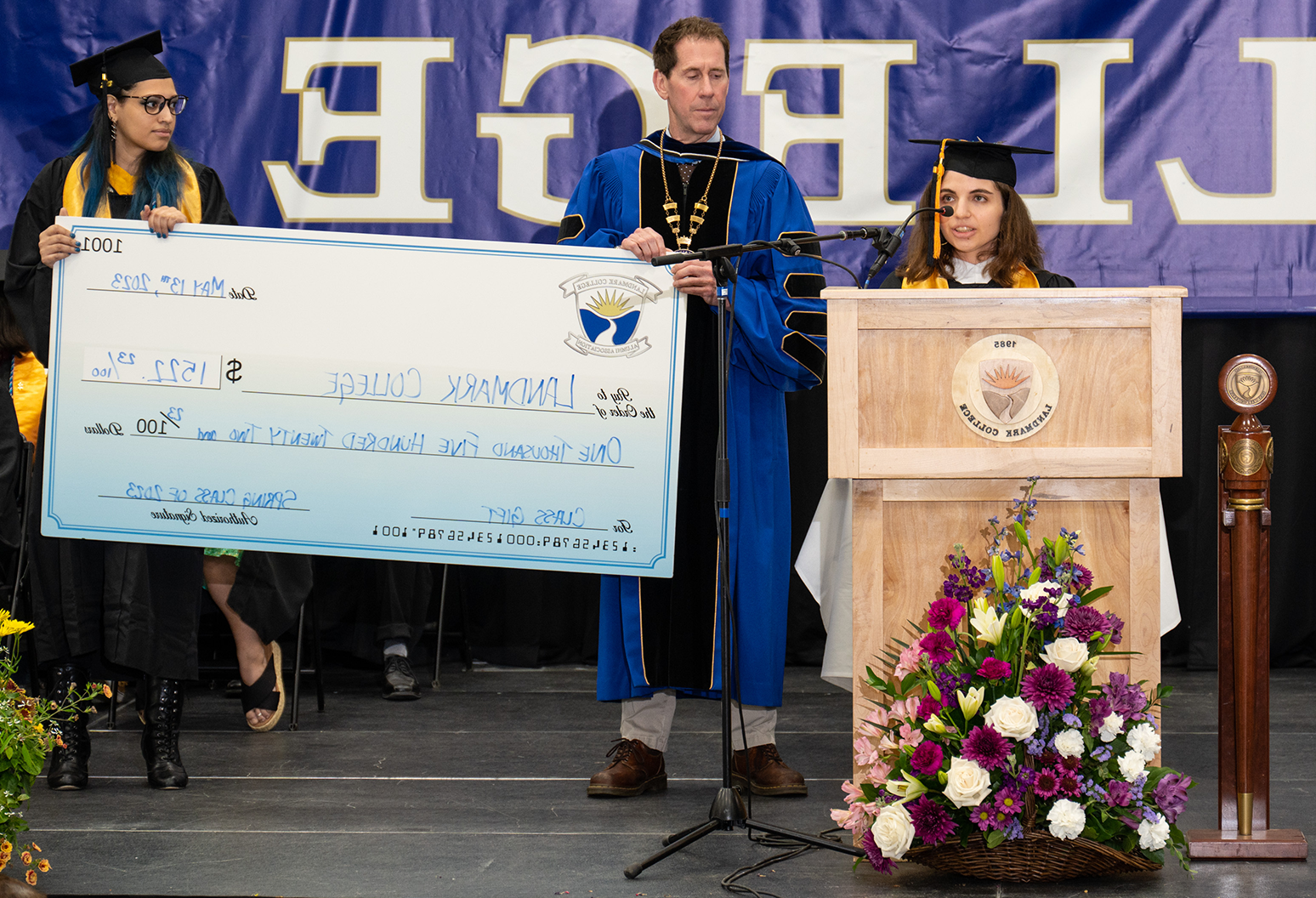 一名女学生站在讲台上发言，而一名男学生和一名女学生拿着一张面额为1美元的超大支票,522.23 