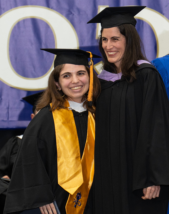 在毕业典礼的舞台上，两名身着毕业礼服的女子微笑着摆姿势拍照